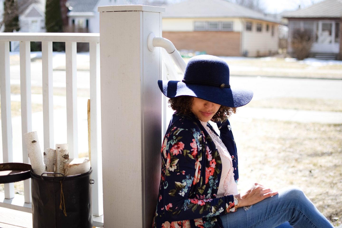 woman sitting down wearing a navy blue floppy hat and a floral cardigan