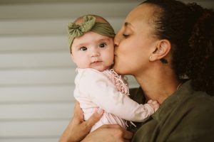close up image of a mixed race woman holding a baby girl and kissing her cheek