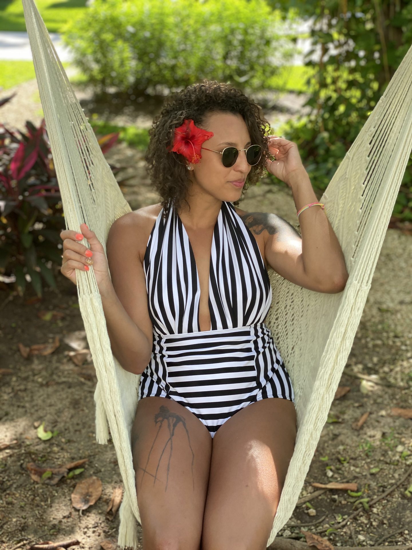 image of a mixed race woman with curly hair sitting in a hammock chair. She is wearing a black and white striped, one-piece swimsuit