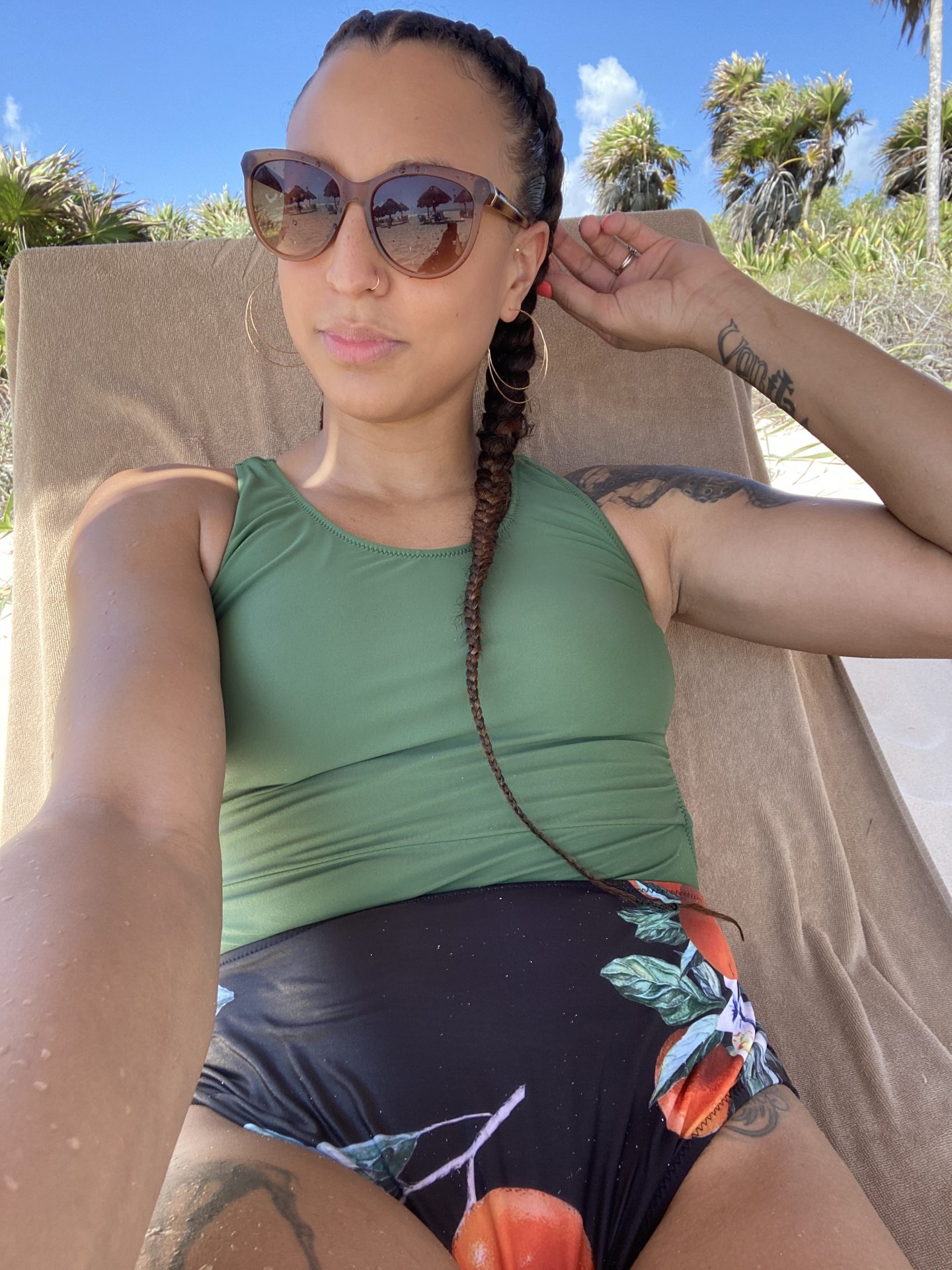 image of a mixed race woman wearing a green and black one-piece swimsuit. There are palm trees behind her.