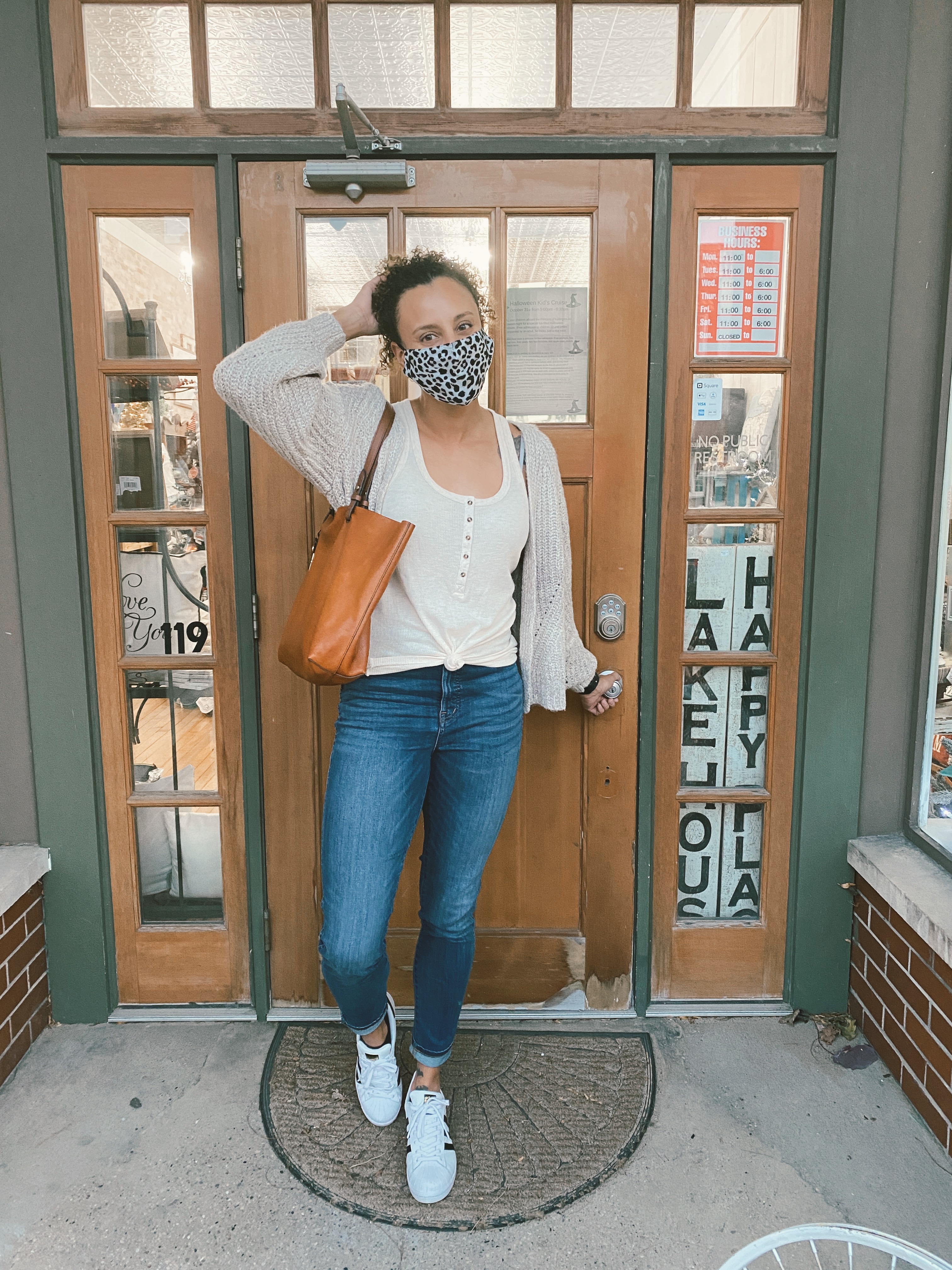 mixed race woman standing outside of a store while wearing a mask