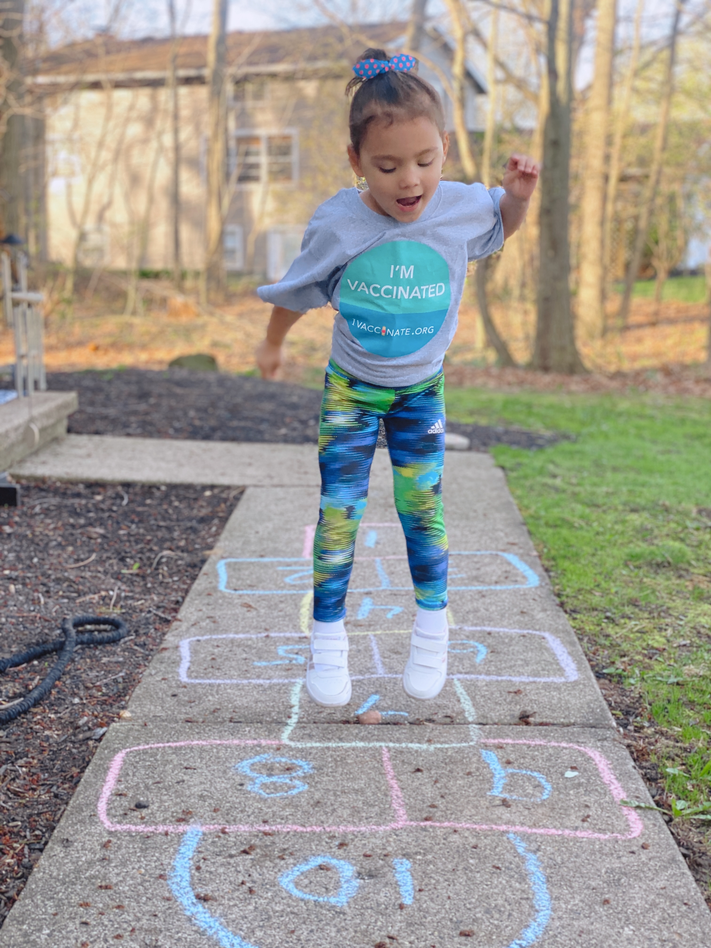 Image of a little girl playing hopscotch. She is mid-jump!